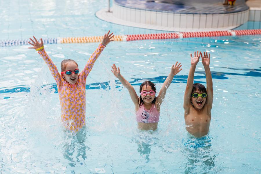 3 children smiling with their arms up in the pool