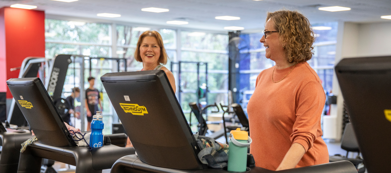 Two women on treadmill facing each other and smiling