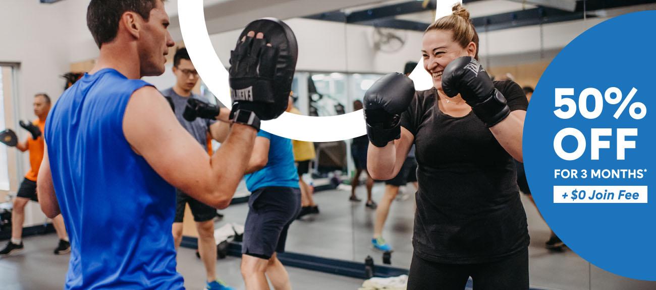 Women smiling, wearing boxing gloves. Blue half circle with text saying "50% off for 3 months +$0 Join fee'