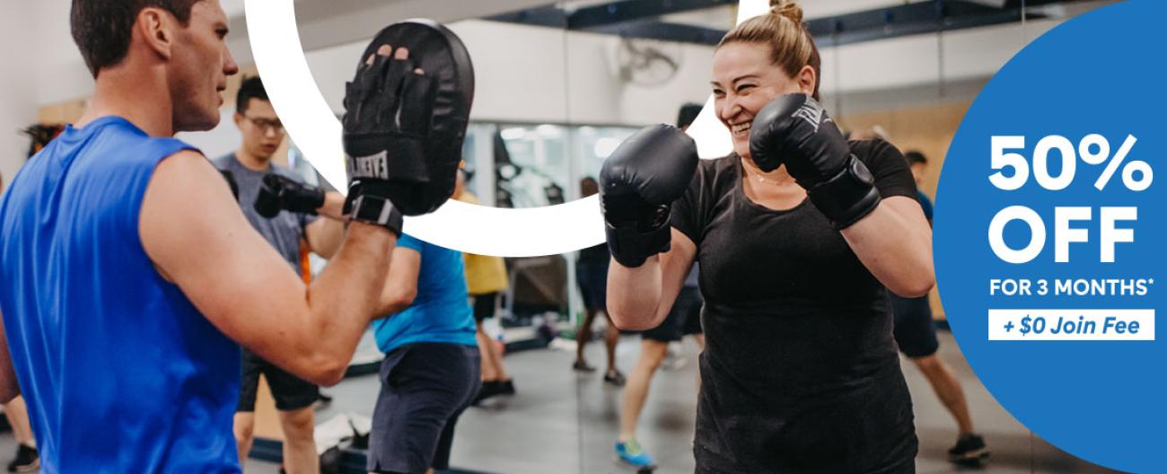 Women smiling, wearing boxing gloves with text to her right ' 50% off for 3 months + $0 Join Fee'